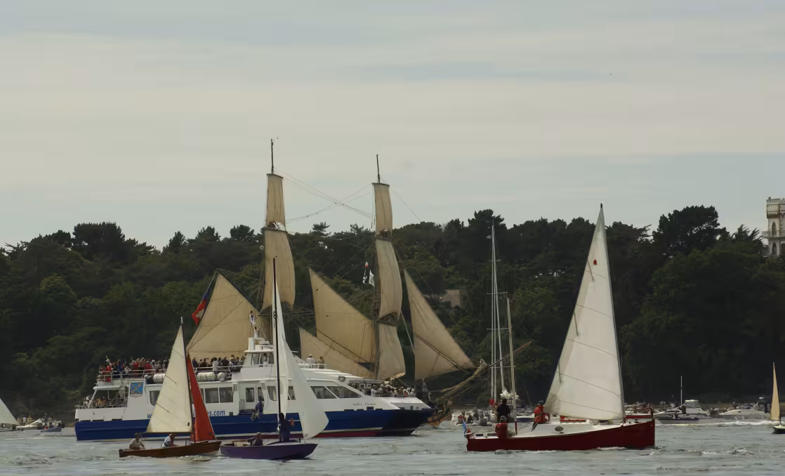 Bateau Izenah entouré de voiliers avec en fond la côte sauvage