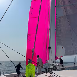Hissage d'une voile rose avec 3 personnes à bord