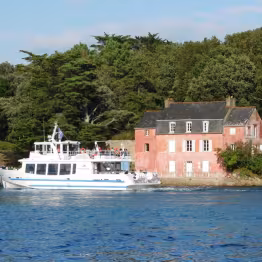 Bateau en mer passant près d'une maison rose en bord de mer